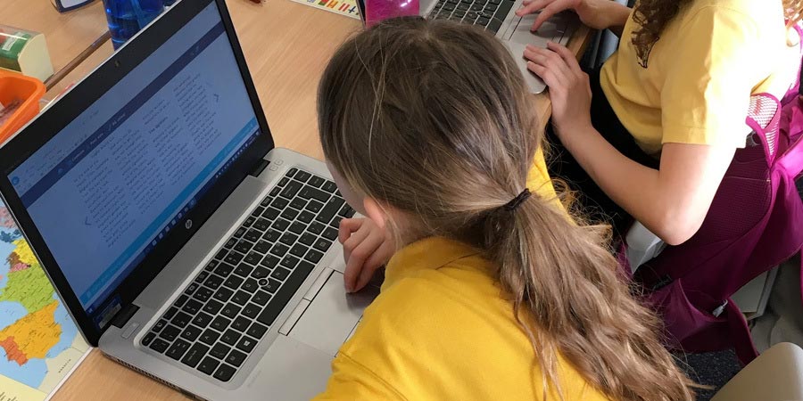 A child in a classroom reading a Giglets book using a laptop.